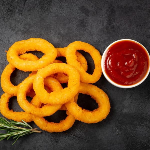 Golden-brown onion rings with a side of ketchup and a sprig of rosemary on a dark surface.