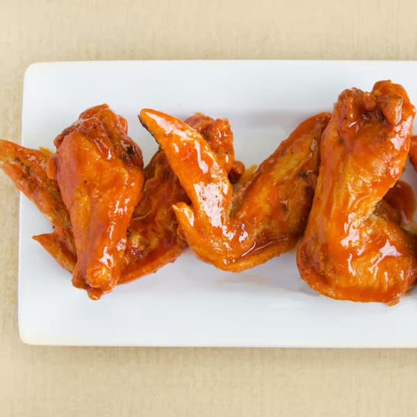 A white rectangular plate holds several glossy, orange-sauced chicken wings from 1930 Classic Kitchen.