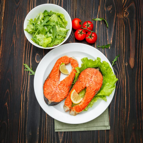 Two salmon fillets with lemon and lime on lettuce, with a side salad and tomatoes.